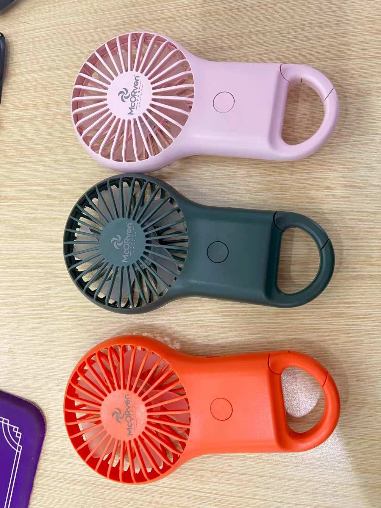 Real Green, Pink and Orange McORven handheld fans showing the integrated carry hooks